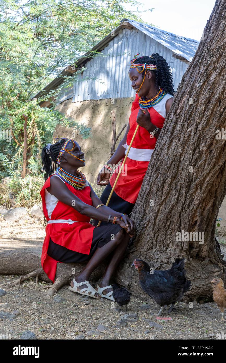 Mann des Njemps-Stammes mit federverziertem Perlenkopfschmuck und kariertem Wickeltuch am Ufer des Sees zwischen Wasserhyazinthen, See Baringo, Kenia Stockfoto