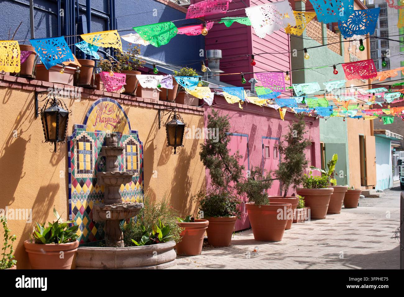 San Antonio, Texas, USA - März 2025: Papel-picado-Banner über dem Gehweg an pastellrosa und orangefarbenen Fassaden am Historic Market Square, El Mercado. Stockfoto