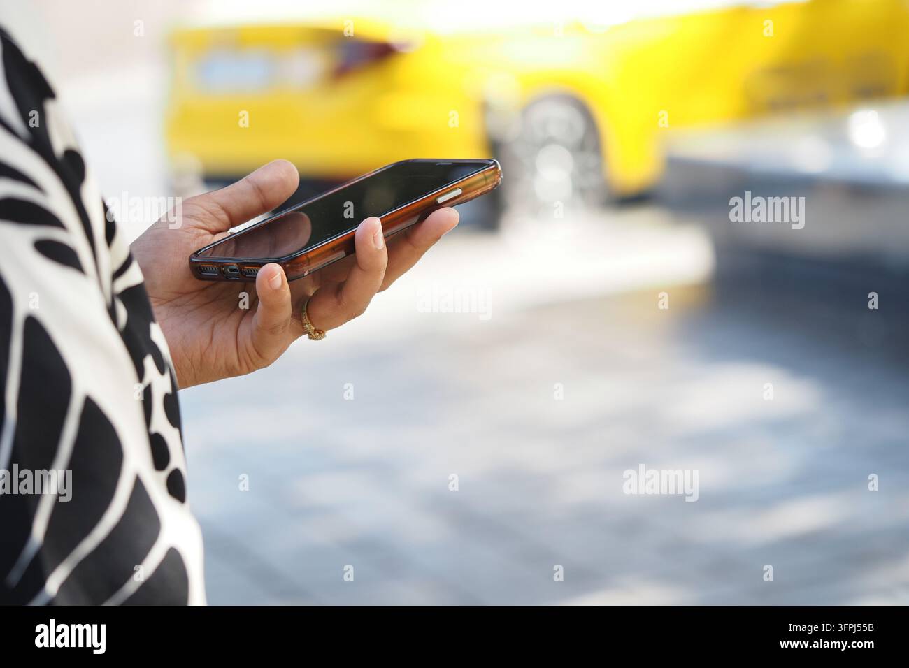 Eine Frau steht mit einem Smartphone in der Hand neben geparkten gelben Autos auf einem Parkplatz Stockfoto