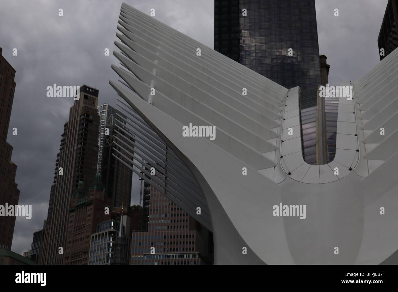 Weißer, flügelartiger Außenbereich des Oculus im World Trade Center Transportation Hub in New York City, mit Wolkenkratzern unter einem bewölkten Himmel. Stockfoto