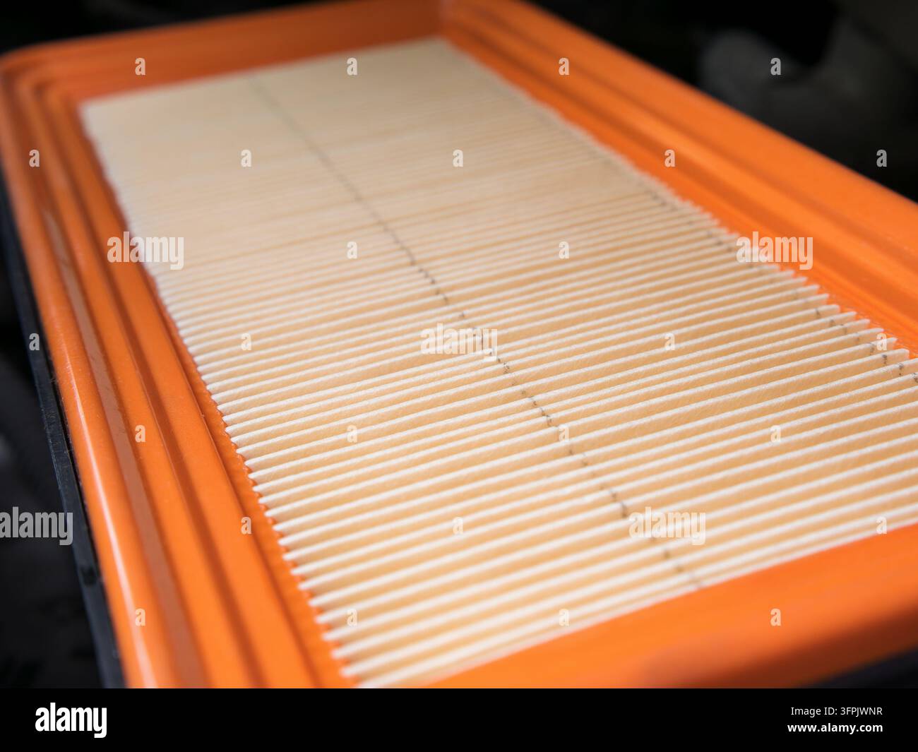 Nahaufnahme eines neuen sauberen Motorluftfilters mit orangefarbenem Gummirahmen. Makroaufnahme von gefaltetem Papierfiltermedium mit scharfen weißen Rippen unter so Stockfoto