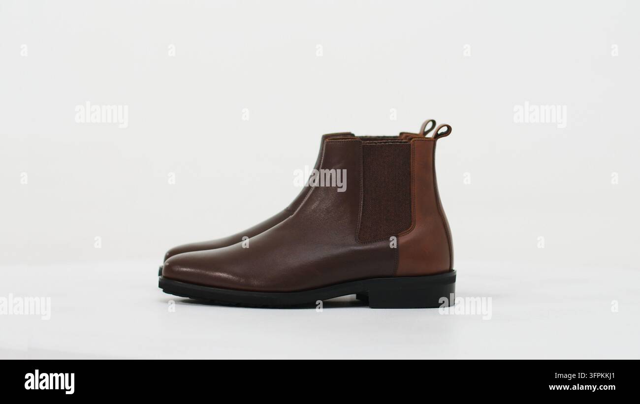 Braune Chelsea-Boots aus Leder mit elastischen Seiteneinsätzen auf weißem Hintergrund, die klassische Herrenmode repräsentieren Stockfoto