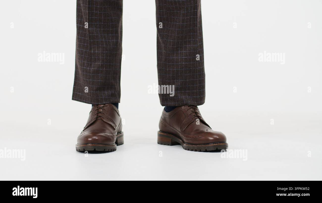 Professioneller Mann im Stehen, der braune Lederschuhe im Brogue-Stil und stilvolle karierte Hosen trägt, und elegante Businessmode präsentiert Stockfoto
