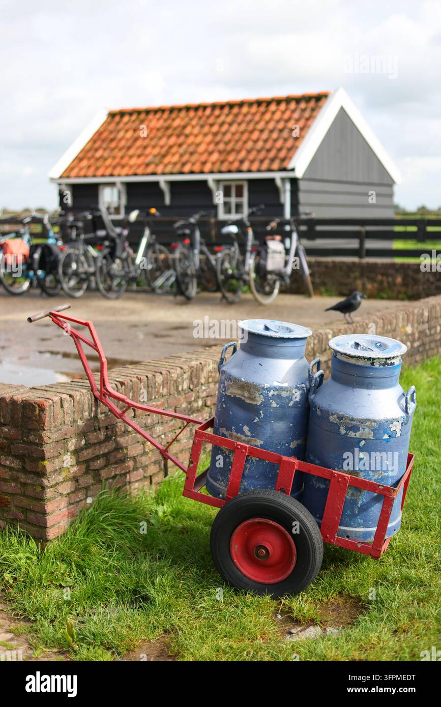 Vintage-Milchkantern auf einem roten Handkarren auf einem niederländischen Bauernhof veranschaulichen die traditionelle Milcherzeugung, das ländliche Erbe und die lokale Lebensmittelkultur. Stockfoto