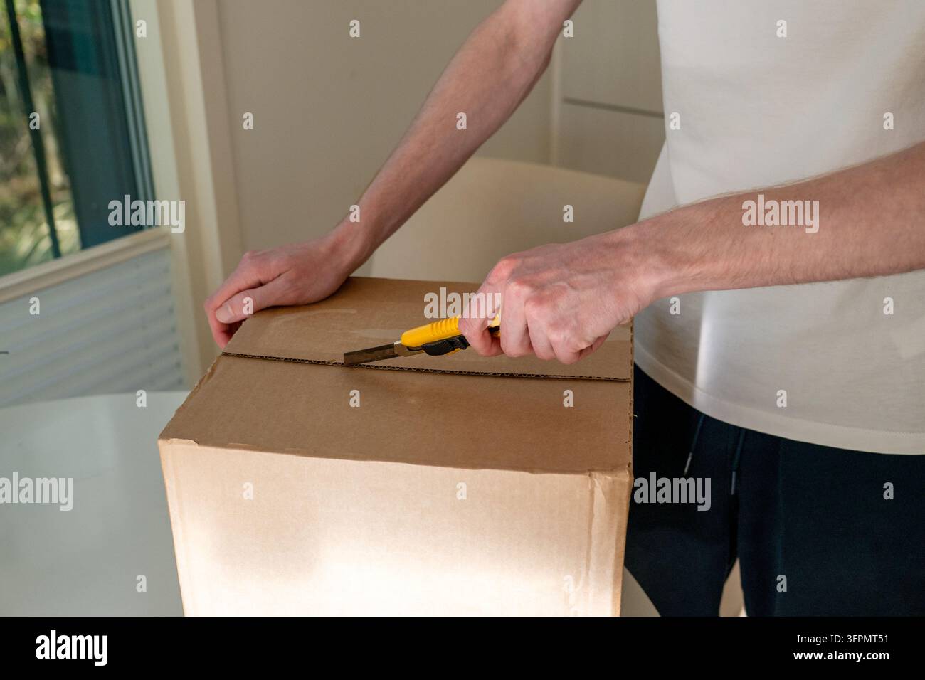 Mann schneidet eine Kartonversandbox mit einem Universalmesser zu Hause auf Stockfoto