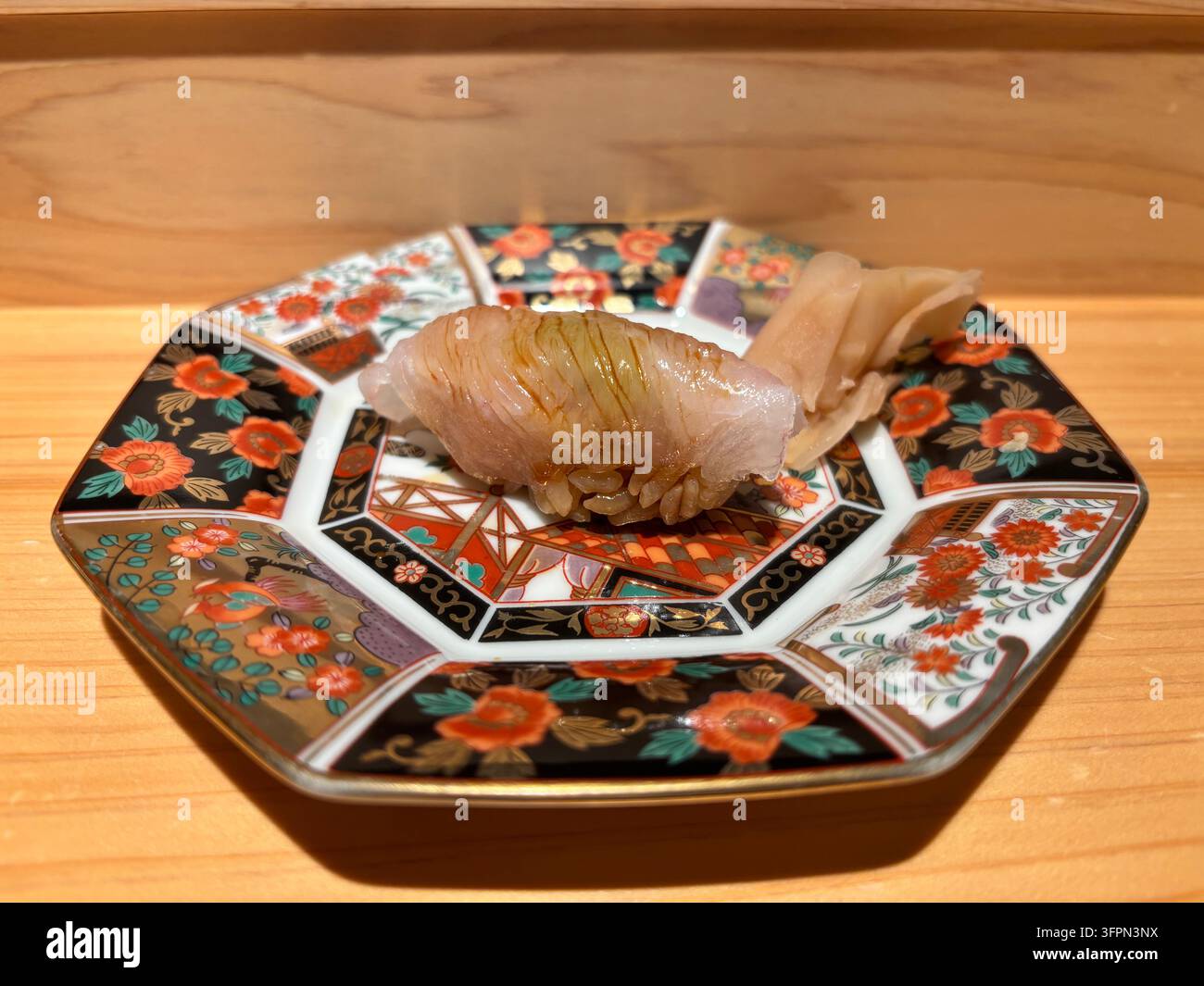 Langzahn-Groppe Nigiri-Sushi, serviert auf einem traditionellen farbenfrohen Arita-Keramikteller auf Holz in einem japanischen Restaurant. - Smartphone-aufgenommenes Stockfoto