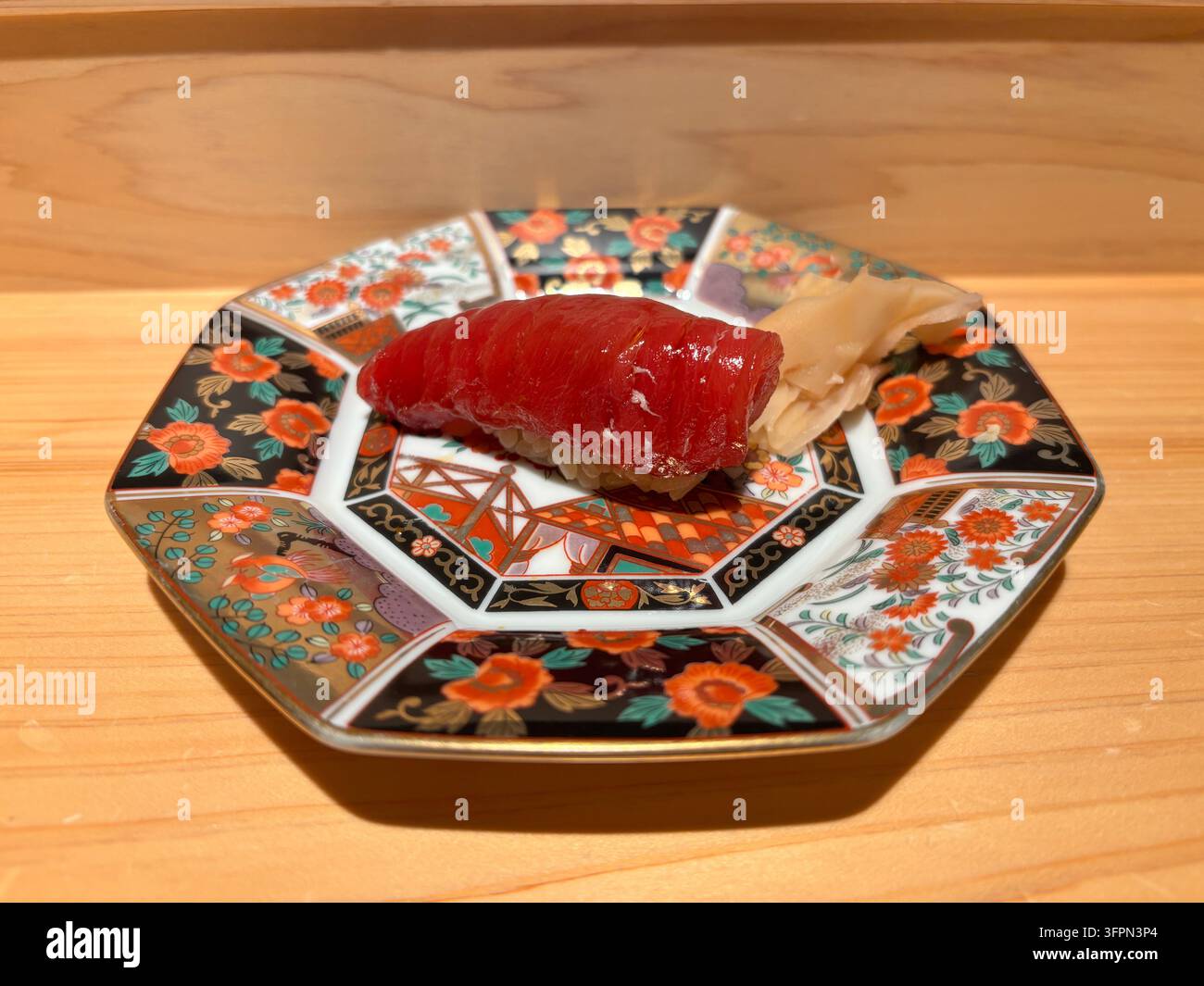 Schlanke Thunfisch-Akami-Nigiri-Sushi, serviert auf einem traditionellen farbenfrohen Arita-Keramikteller auf einer Holztheke in einem Restaurant. - Smartphone-aufgenommenes Stockfoto