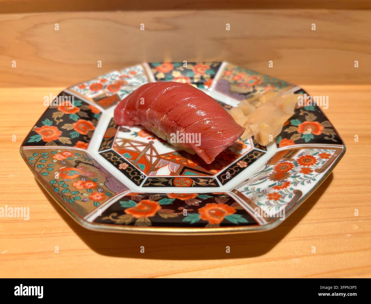 Mittelfettiger Thunfisch-Chutoro-Nigiri-Sushi, serviert auf einem traditionellen bunten Arita-Keramikteller auf einer Holztheke in einem Restaurant. - Smartphone-aufgenommenes Stockfoto