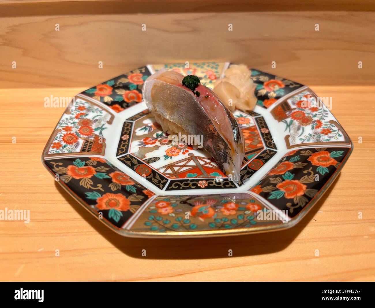 Aji (japanischer Gelbschwanz) Nigiri-Sushi mit Ingwer und grüner Zwiebel, serviert auf einem traditionellen bunten Keramikteller auf einer Holztheke. - Smartphone-aufgenommenes Stockfoto