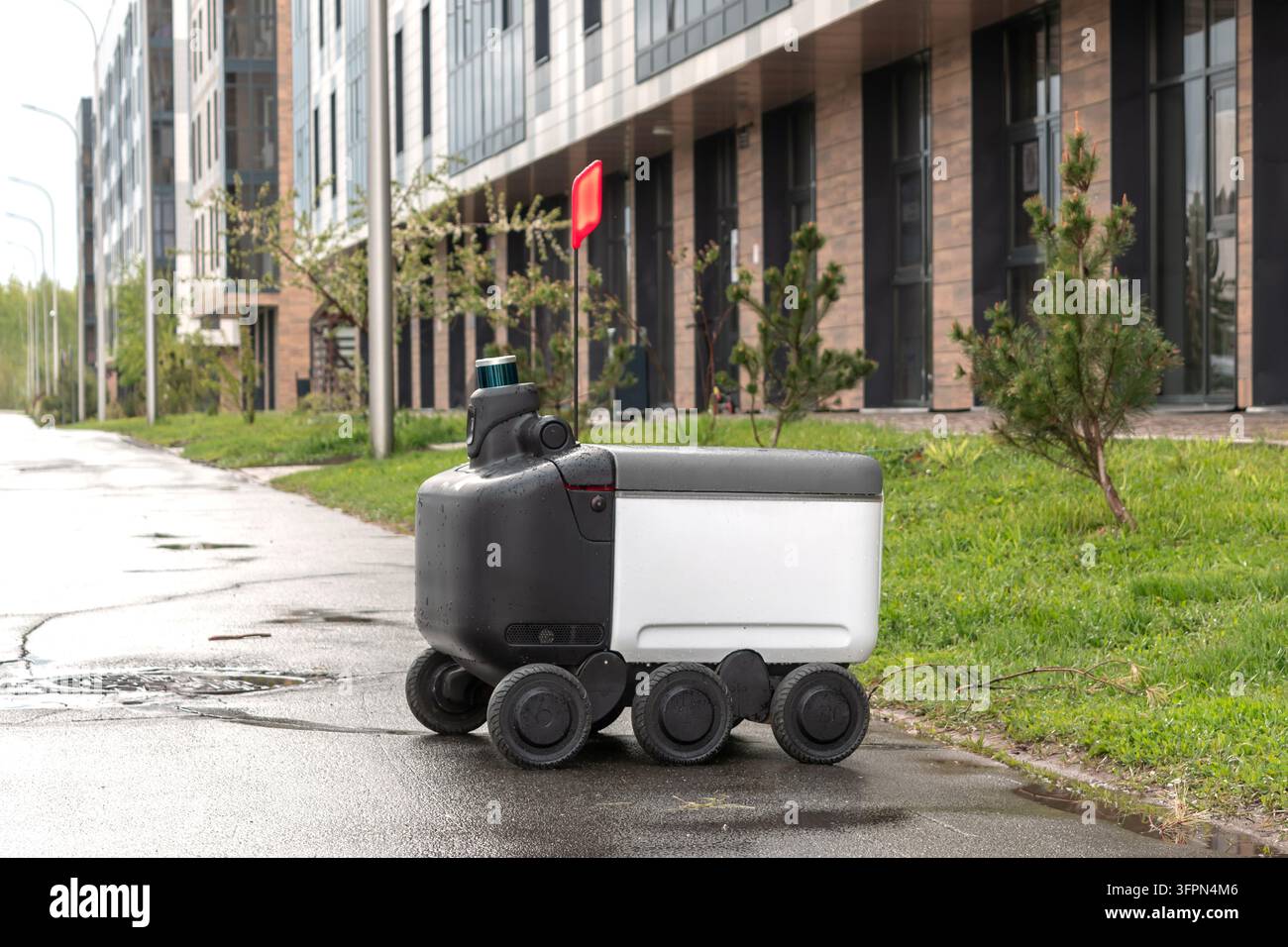 Moderner automatisierter Lieferroboter steht draußen und wartet bei regnerischem Wetter auf eine Bestellung. Modernes Konzept der Lieferung von Waren an den Kunden. Stockfoto