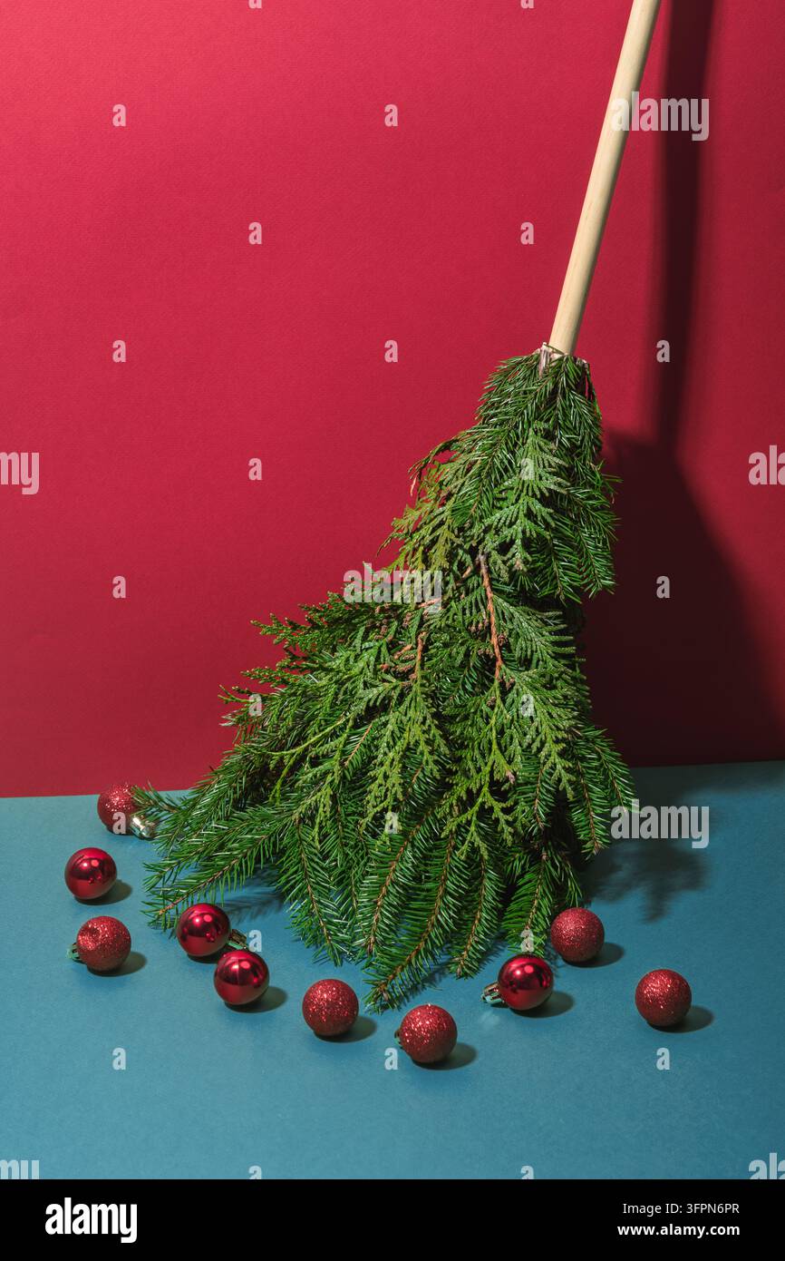 Kreativer Besen aus Tannenwedeln mit verstreuten roten Weihnachtskugeln auf farbenfrohem Hintergrund bringt festliche und verspielte Weihnachtsstimmung. Stockfoto