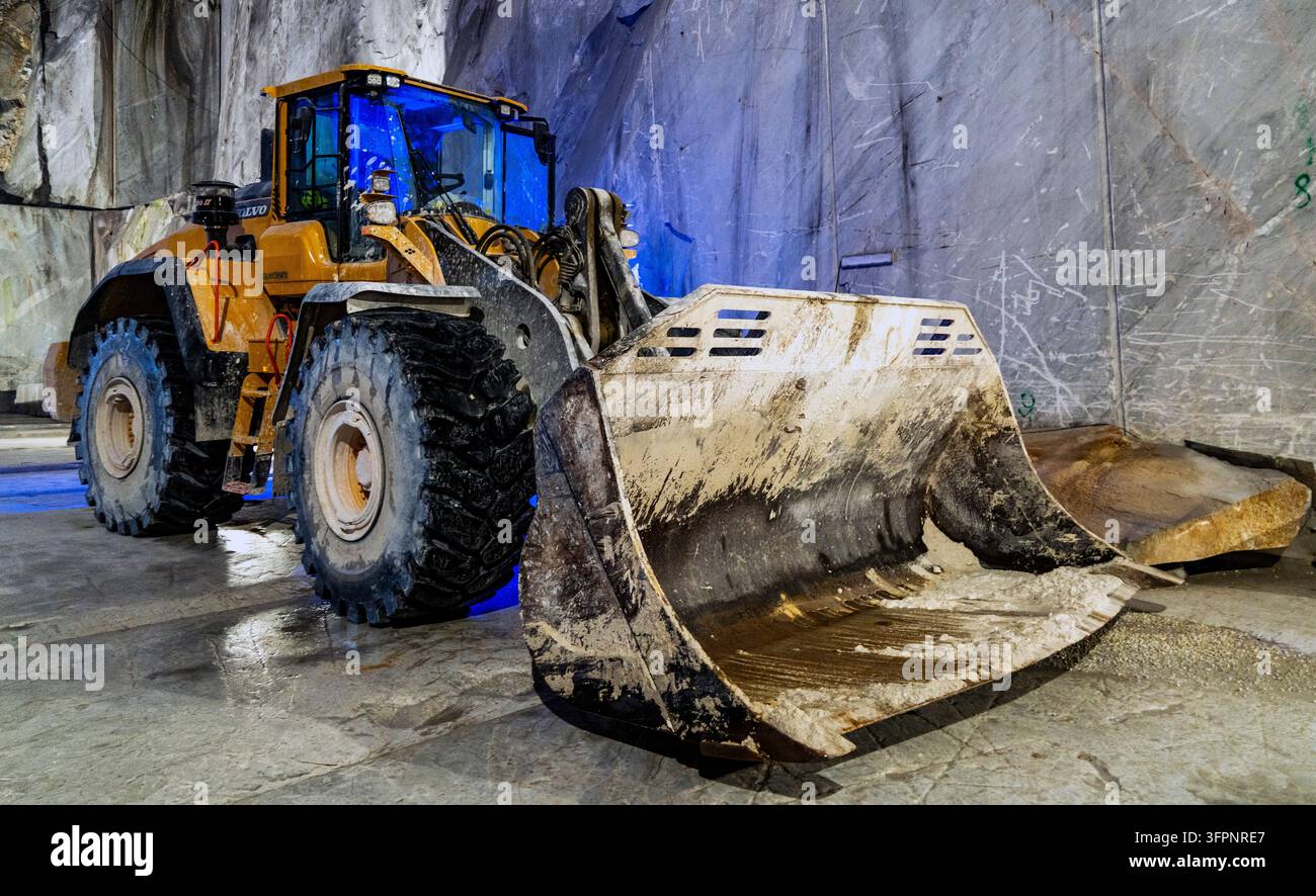 Gelber Radlader mit einem großen schmutzigen Bagger in einem unterirdischen Bergwerk oder Steinbruchtunnel mit rauen Felswänden und nassem Betonboden geparkt Stockfoto