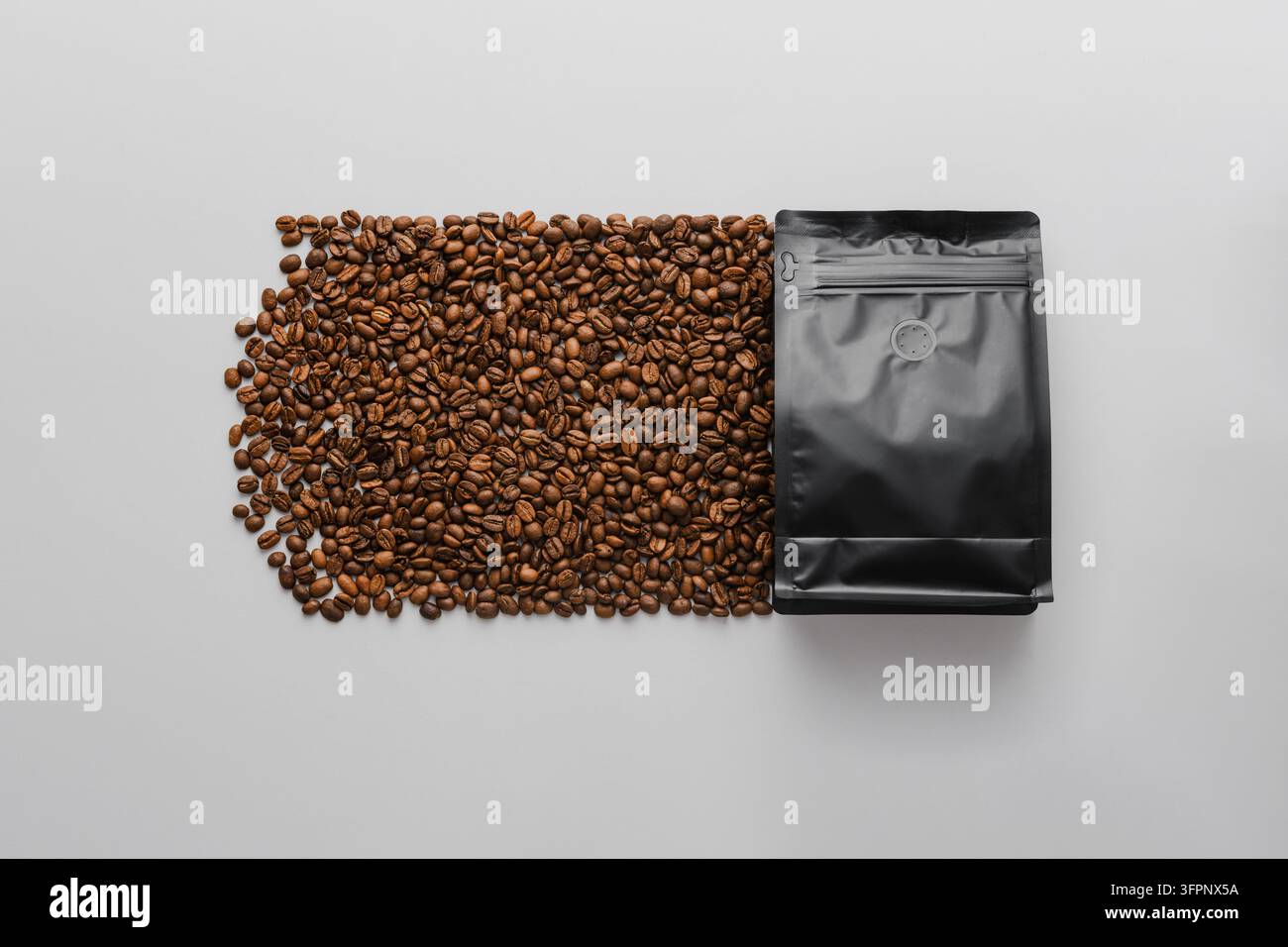 Schwarzer Kaffebeutel erzeugt eine fließende Spur gerösteter Bohnen auf weißem Hintergrund und präsentiert ein kreatives Verpackungs-Mockup für Branding-Nutzung. Stockfoto