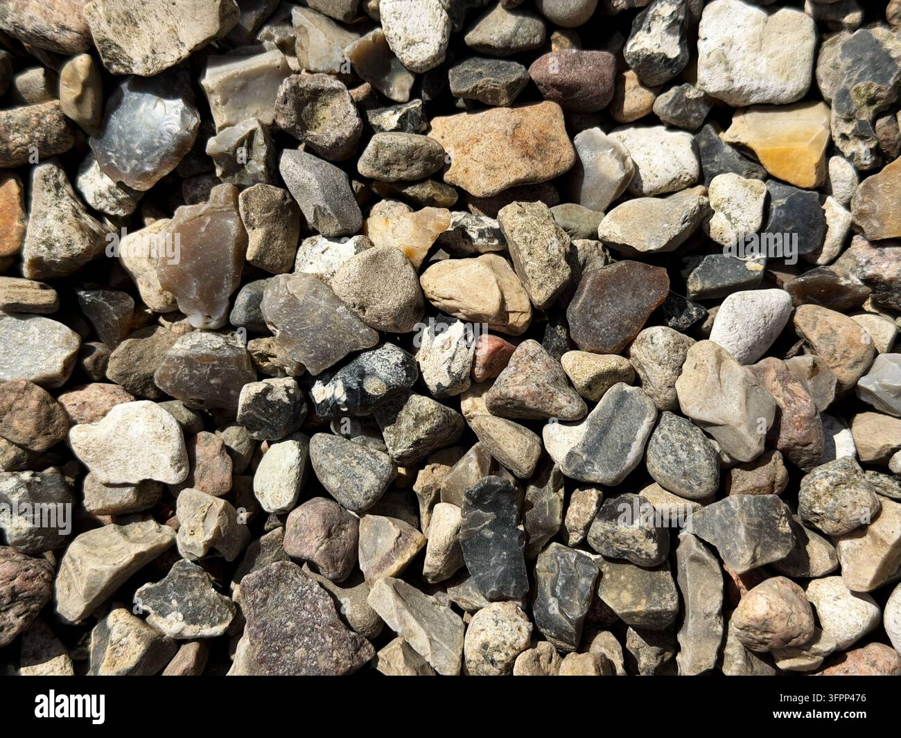 Nahaufnahme von natürlichen Kieselsteinen und kleinen Steinen in verschiedenen Formen, Größen und erdigen Farben, die eine detaillierte Steintекстur und einen Hintergrund bilden. - Smartphone-aufgenommenes Stockfoto