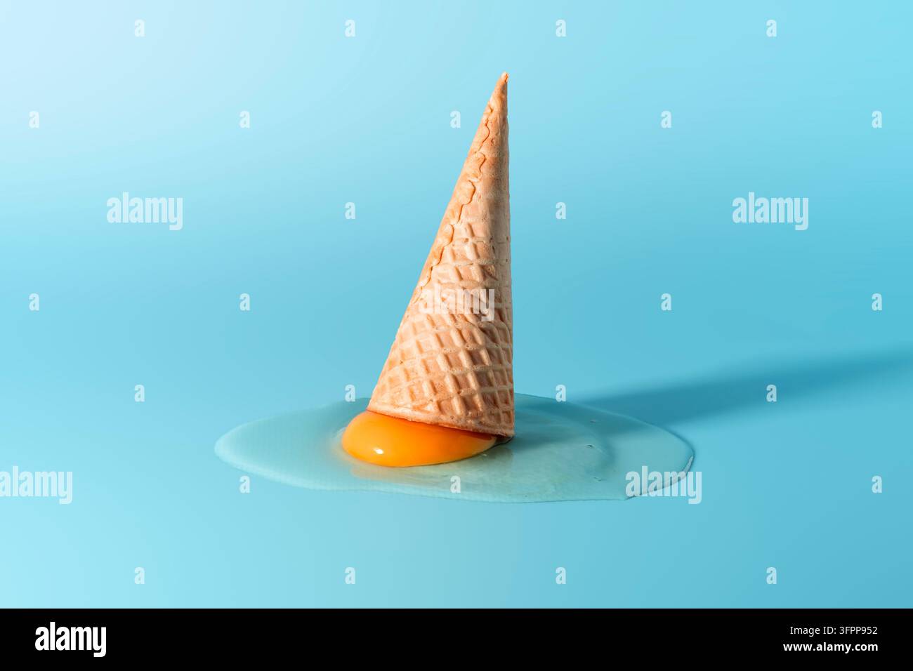 Waffeltüte steht über rohem Eigelb auf heller blauer Oberfläche und hebt die surreale Kombination aus Dessertform und Frühstückselement hervor. Stockfoto