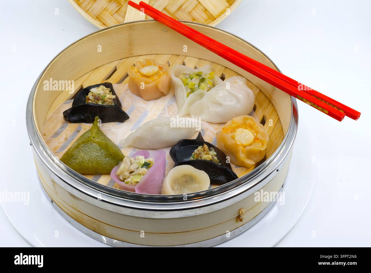 Asiatische Küche. Vielfalt an gedämpften Teigtaschen in einem Bambusdampfer: schwarze, grüne, weiße und orange Sorten. Stockfoto