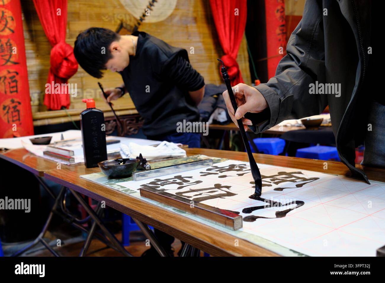 Kalligraphie-Workshop-Szene mit zwei Teilnehmern, die mit Tintenbürsten auf Reispapier schreiben. Hanoi. Vietnam. Stockfoto