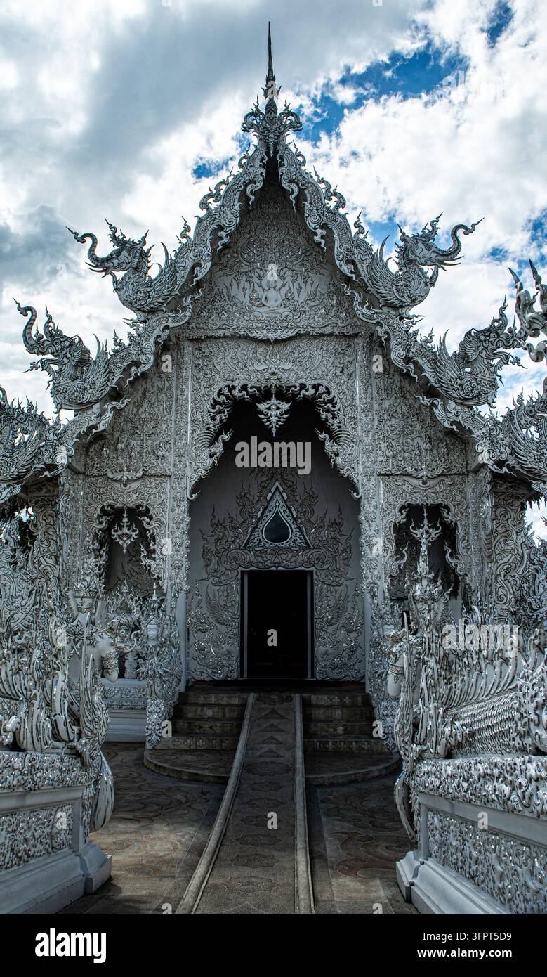 Weißer Tempel mit aufwendigen Designs und dunklem Eingang unter bewölktem Himmel, Chiang Rai, Thailand Stockfoto