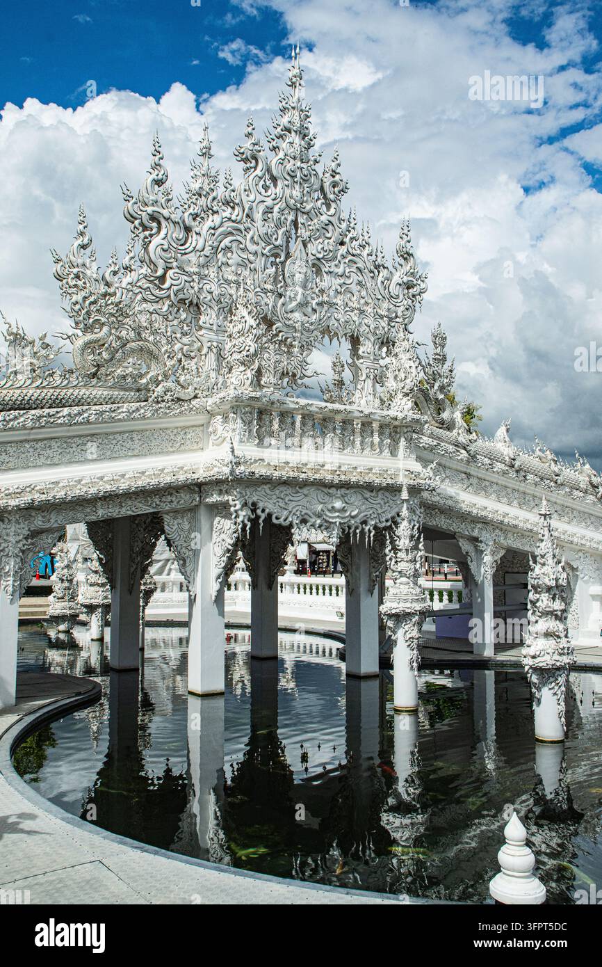 Komplexe weiße Tempelstruktur mit spiegelndem Wasser unter einem bewölkten Himmel, Chiang Rai, Thailand Stockfoto