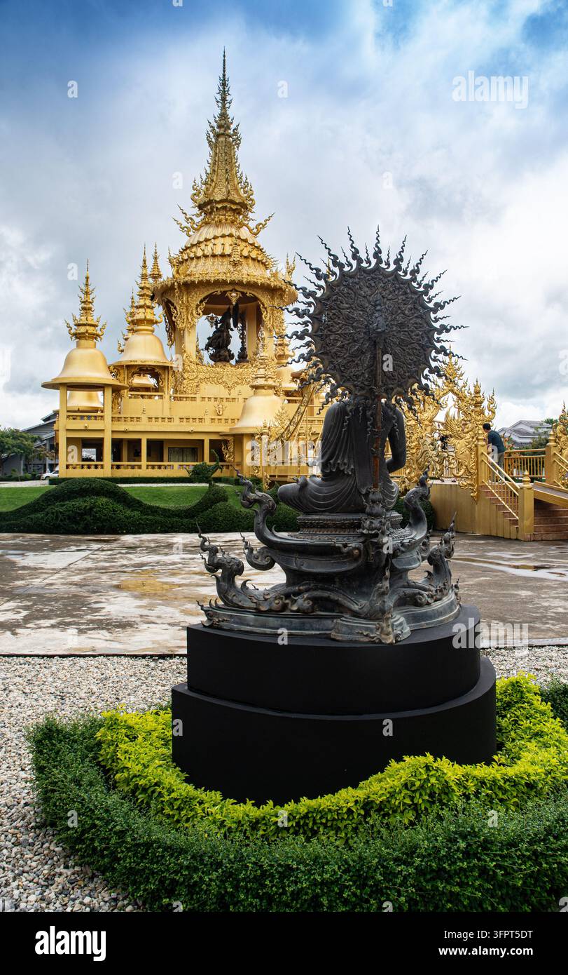 Goldener Tempel und Bronzestatue vor bewölktem Himmel in Thailand, Chiang Rai, Thailand Stockfoto
