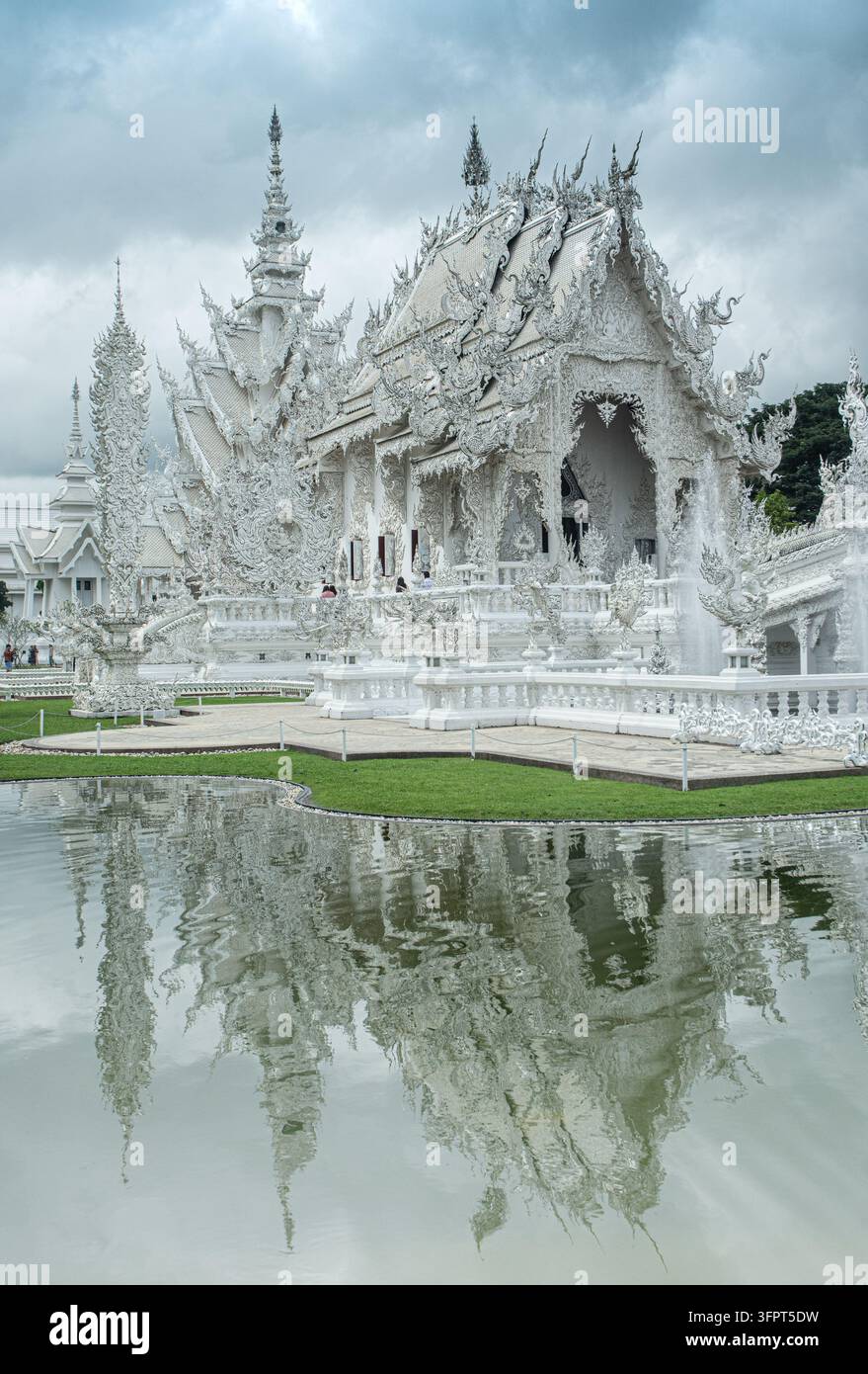Architektonische Details eines weißen Tempels, der sich unter bewölktem Himmel im Wasser spiegelt, Chiang Rai, Thailand Stockfoto