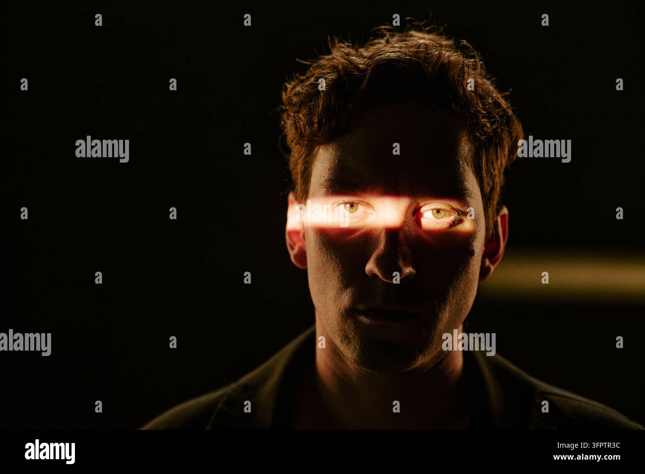 Porträt eines Mannes mit Lichtstrahl über den Augen in einem dunklen Studio Stockfoto