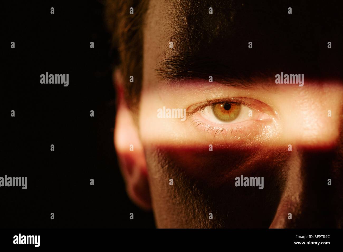 Porträt eines Mannes mit Lichtstrahl über dem Auge, der in die Kamera schaut Stockfoto