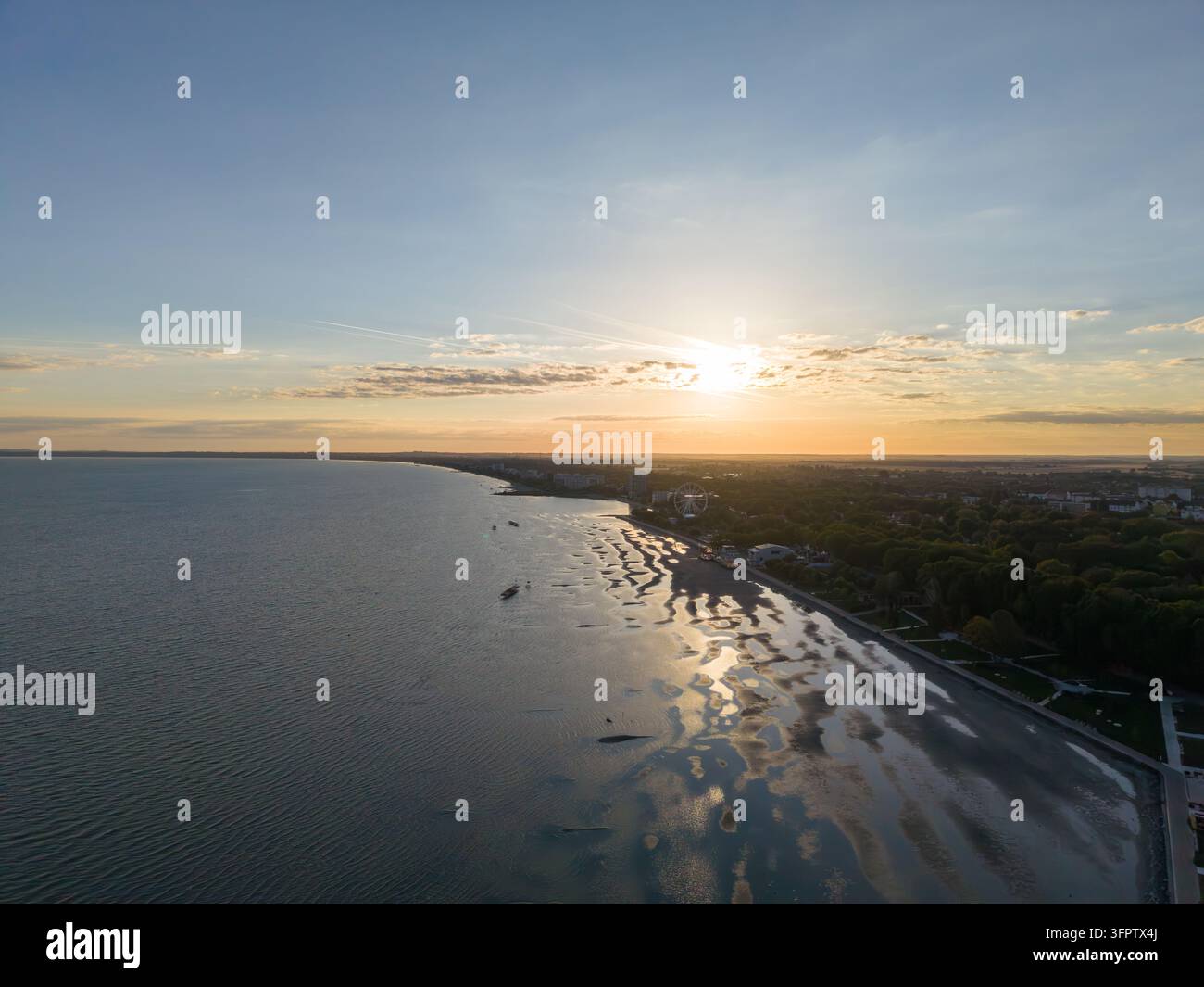 Ufer des Balaton glüht bei Sonnenuntergang, mit goldenem Licht, das sich über flaches Wasser und nassen Sand spiegelt. Ungarisches Seeuferresort liegt jenseits der Kurve Stockfoto
