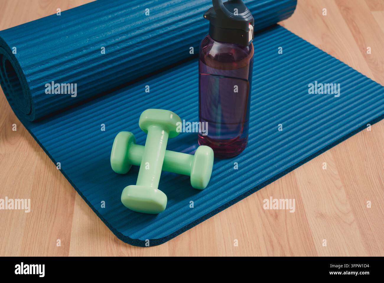 Gerollte Matte, Hanteln und Wasserflasche für ein komplettes Home-Fitness-Workout vorbereitet Stockfoto