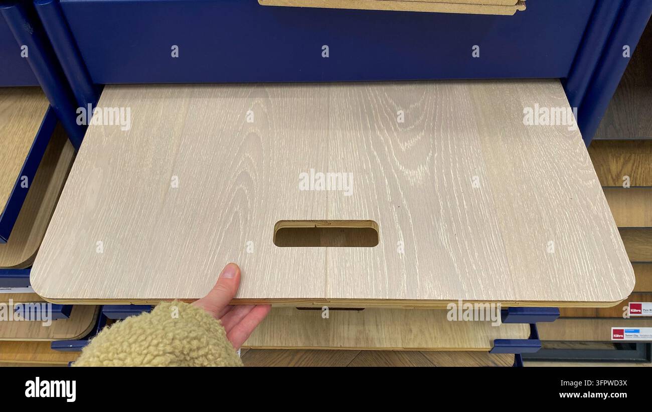 Kunde betrachtet hellgrauen Holzoptik-Laminatbodenmuster auf Schiebeausstellungsregal im Baumarkt Stockfoto