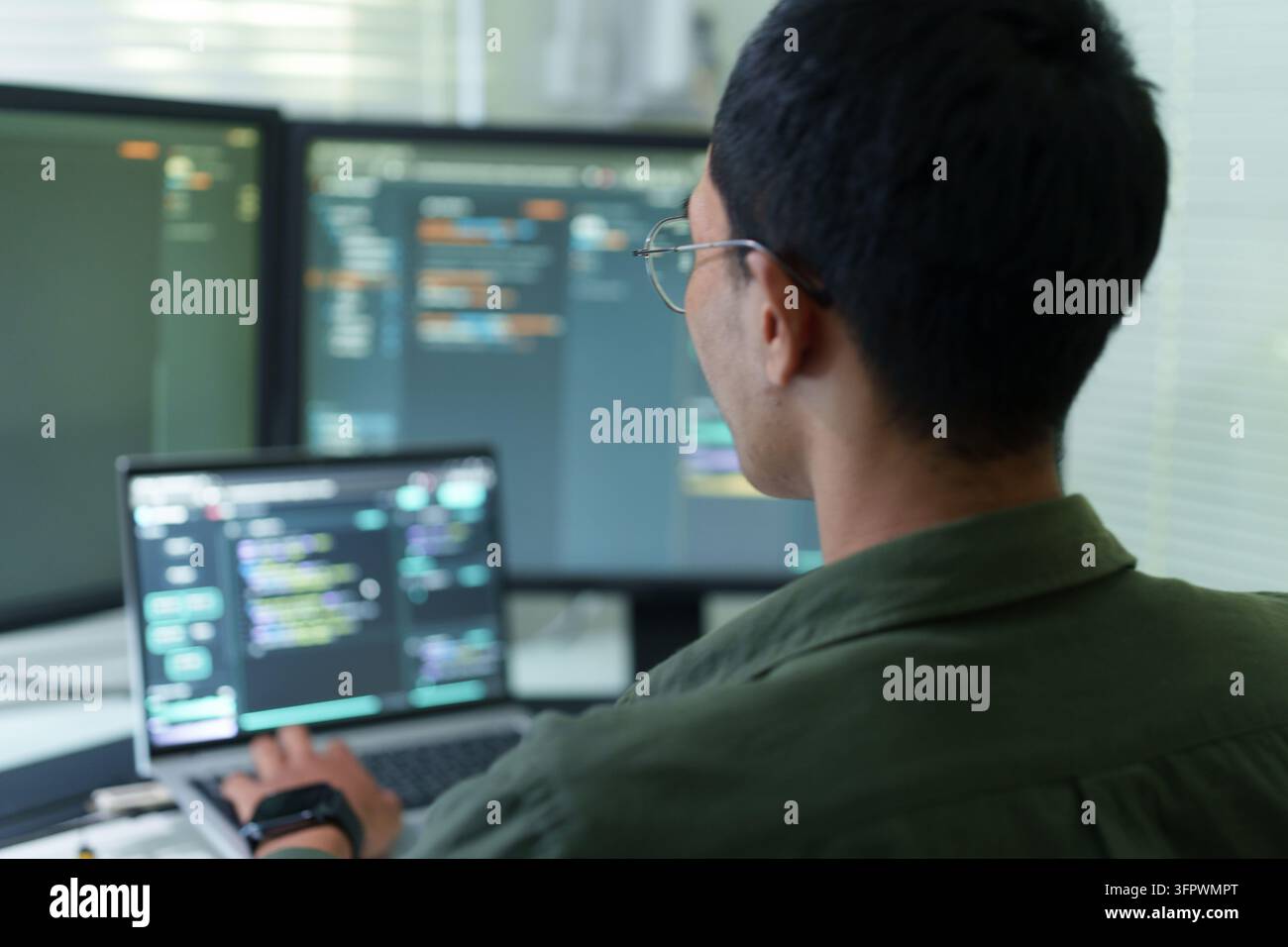 Männlicher Entwickler schreibt Code auf mehreren Monitoren Stockfoto