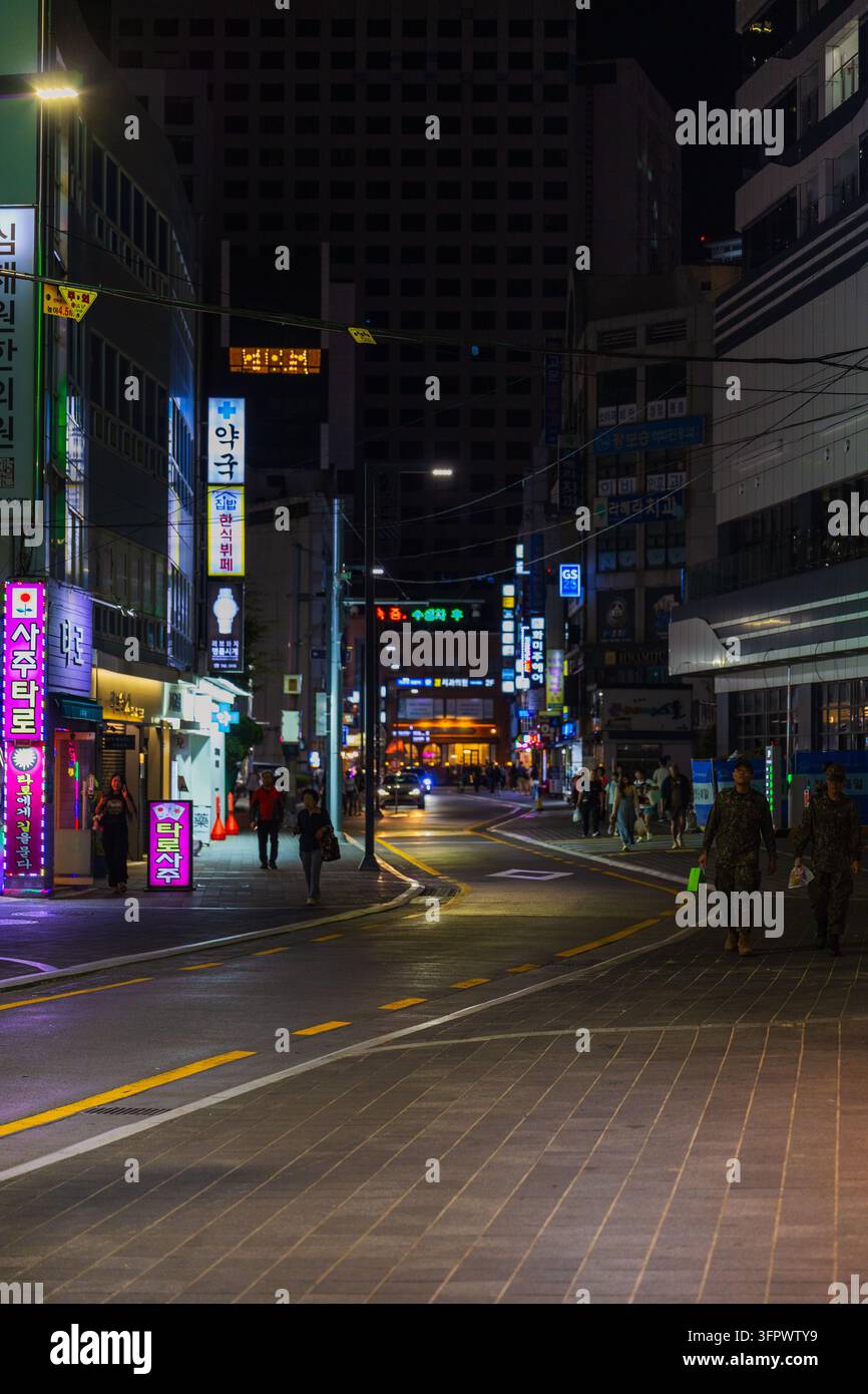 Südkorea, Busan – 21. Sep. 2026: Nachtstraße in Haeundae mit Neonreklamen, Apothekenfassade und Fußgängern in Militäruniformen Stockfoto