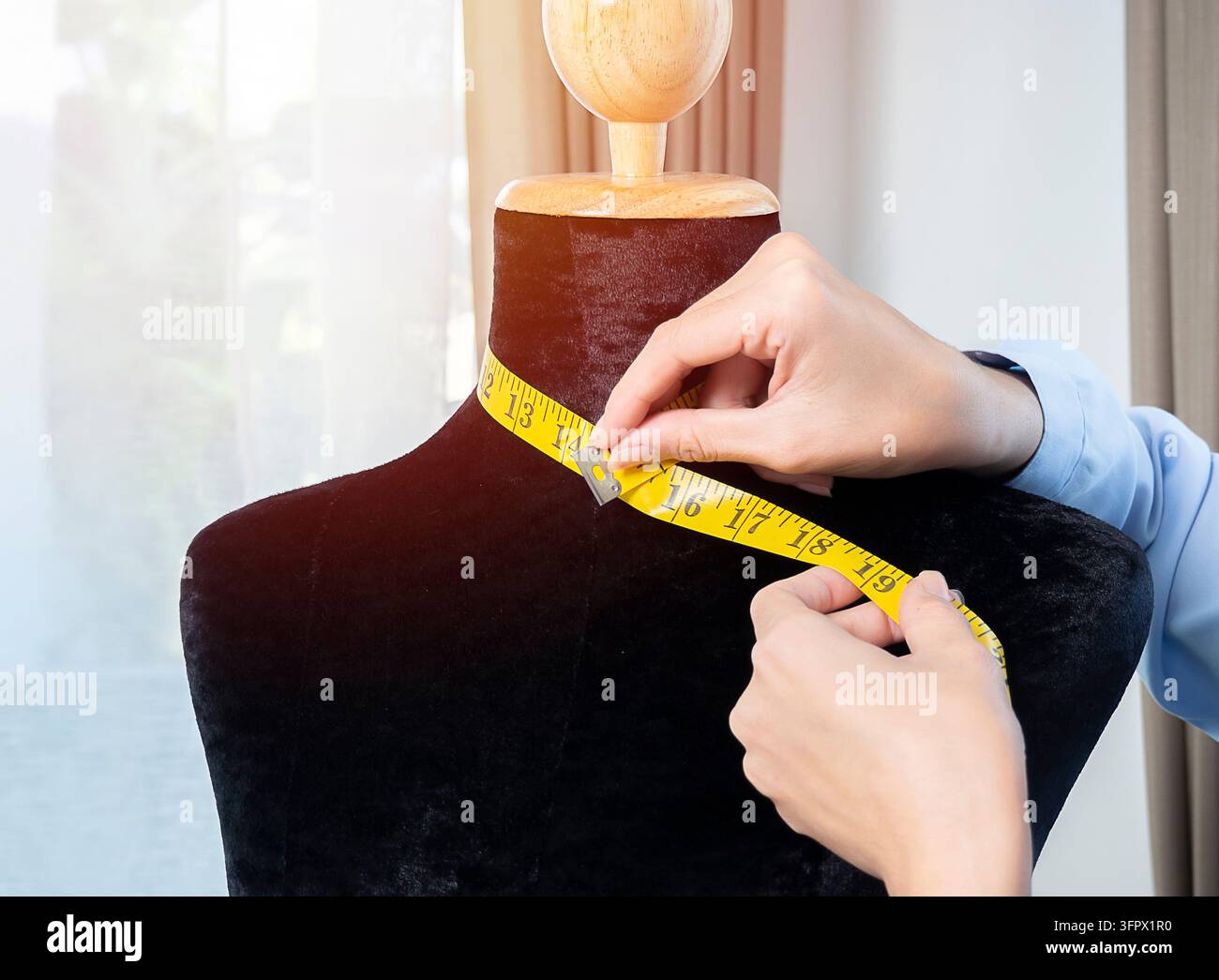 Nahaufnahme der Hände einer jungen asiatischen Modedesignerin, die an einer Schaufensterpuppe in ihrem Atelier Maß nimmt Stockfoto