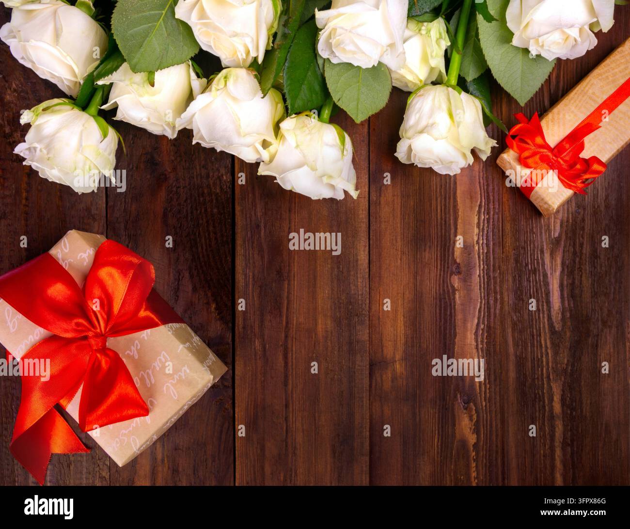 viele weiße Rosen auf einem dunklen Holzgrund mit einem Geschenk und einer roten Schleife, eine sanfte Tagespostkarte, ein Valentinstag oder ein Frauentag. Grußkarte. Ort Stockfoto