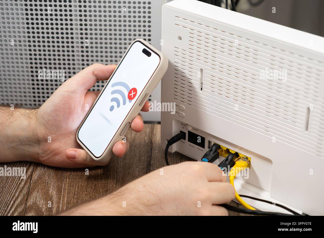 Die Person inspiziert Netzwerkkabel, die in einen modernen Heimrouter eingesteckt sind, während sie ein mobiles Gerät überprüft, das eine schlechte Konnektivität anzeigt, und illustriert eine Technik Stockfoto