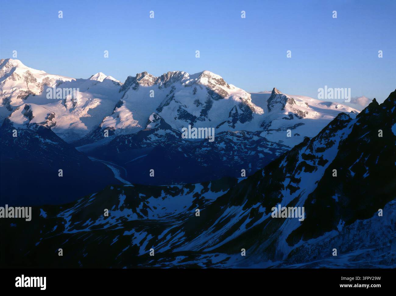 Ein majestätischer Blick auf schneebedeckte Berge, die in dem sanften Licht der Morgendämmerung gebadet sind. Die Szene vermittelt ein Gefühl von Ruhe und Erhabenheit. Stockfoto