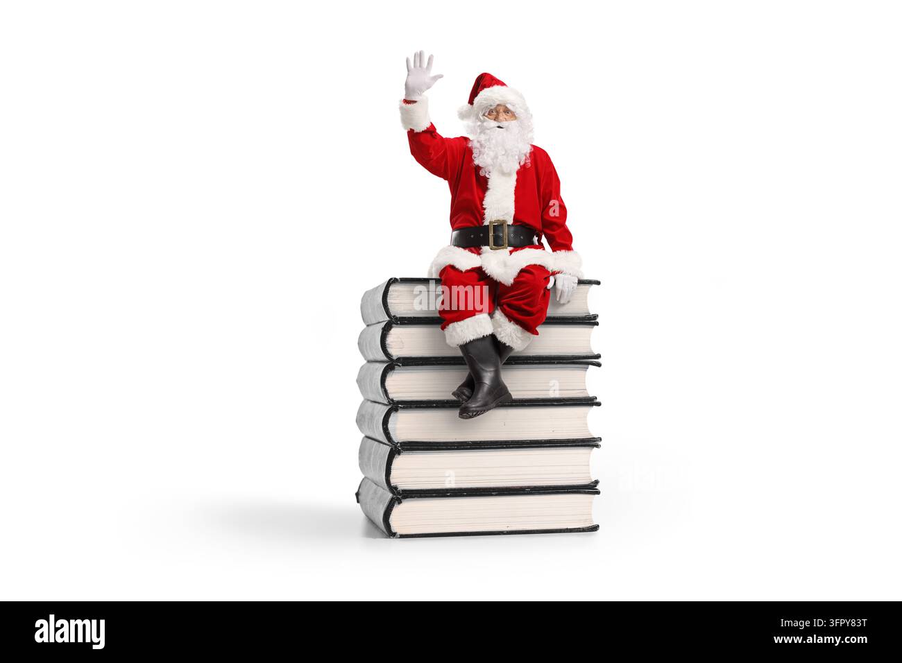 Vollständige Darstellung von Santa Claus, der auf einem Stapel Bücher sitzt und isoliert auf weißem Hintergrund winkt Stockfoto