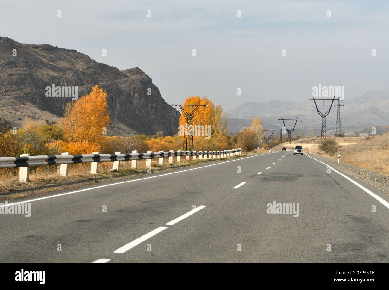 Zweispurige Autobahn mit Leitplanke, Herbstbäumen und Strommasten durchquert ein Bergtal in Armenien, Südkaukasus Stockfoto