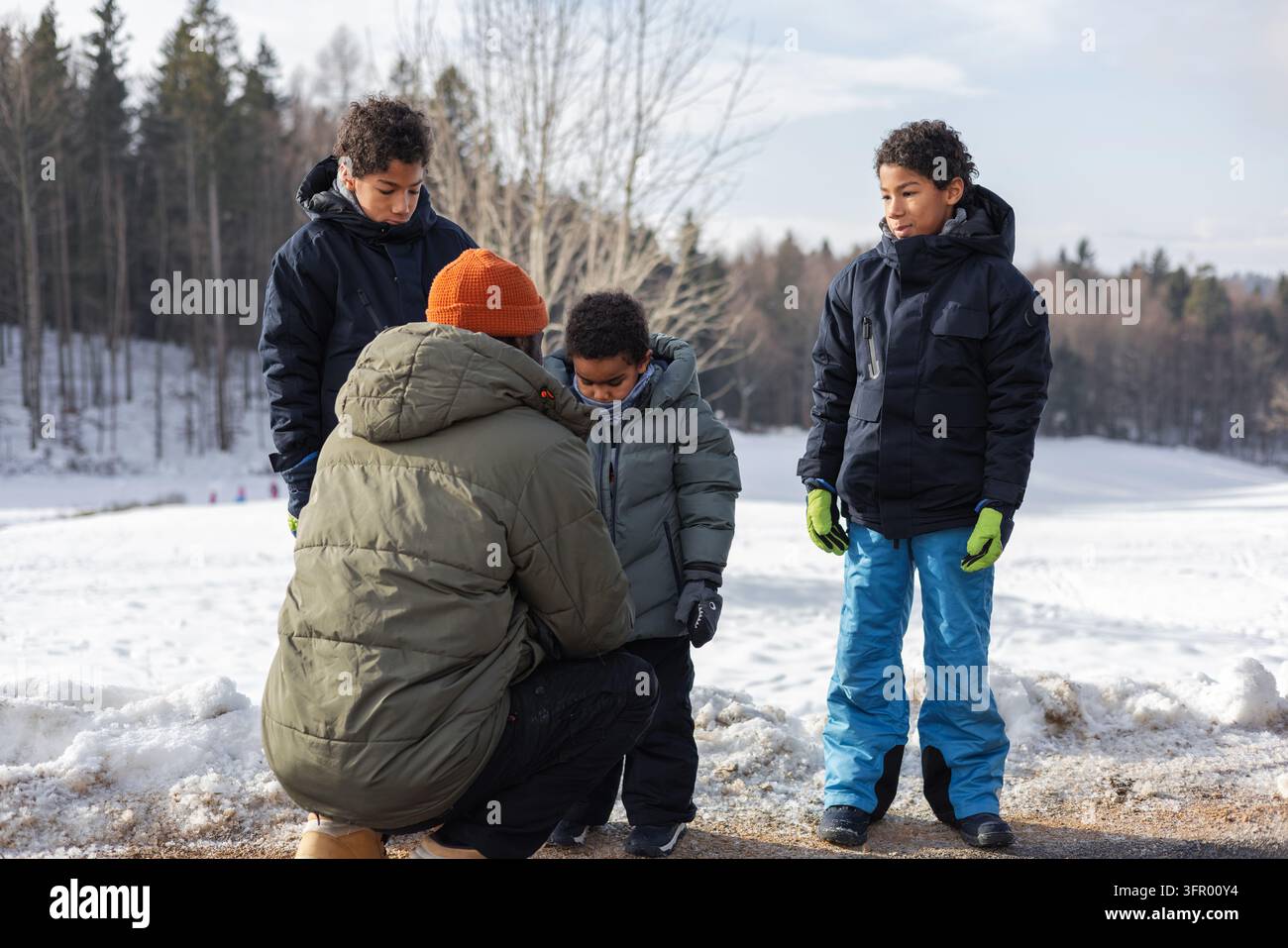 Elternsorge und Zuneigung, afroamerikanischer Vater hilft seinen Söhnen, warme Winterkleidung anzuziehen und sich für Outdoor-Abenteuer im Schnee vorzubereiten. Stockfoto