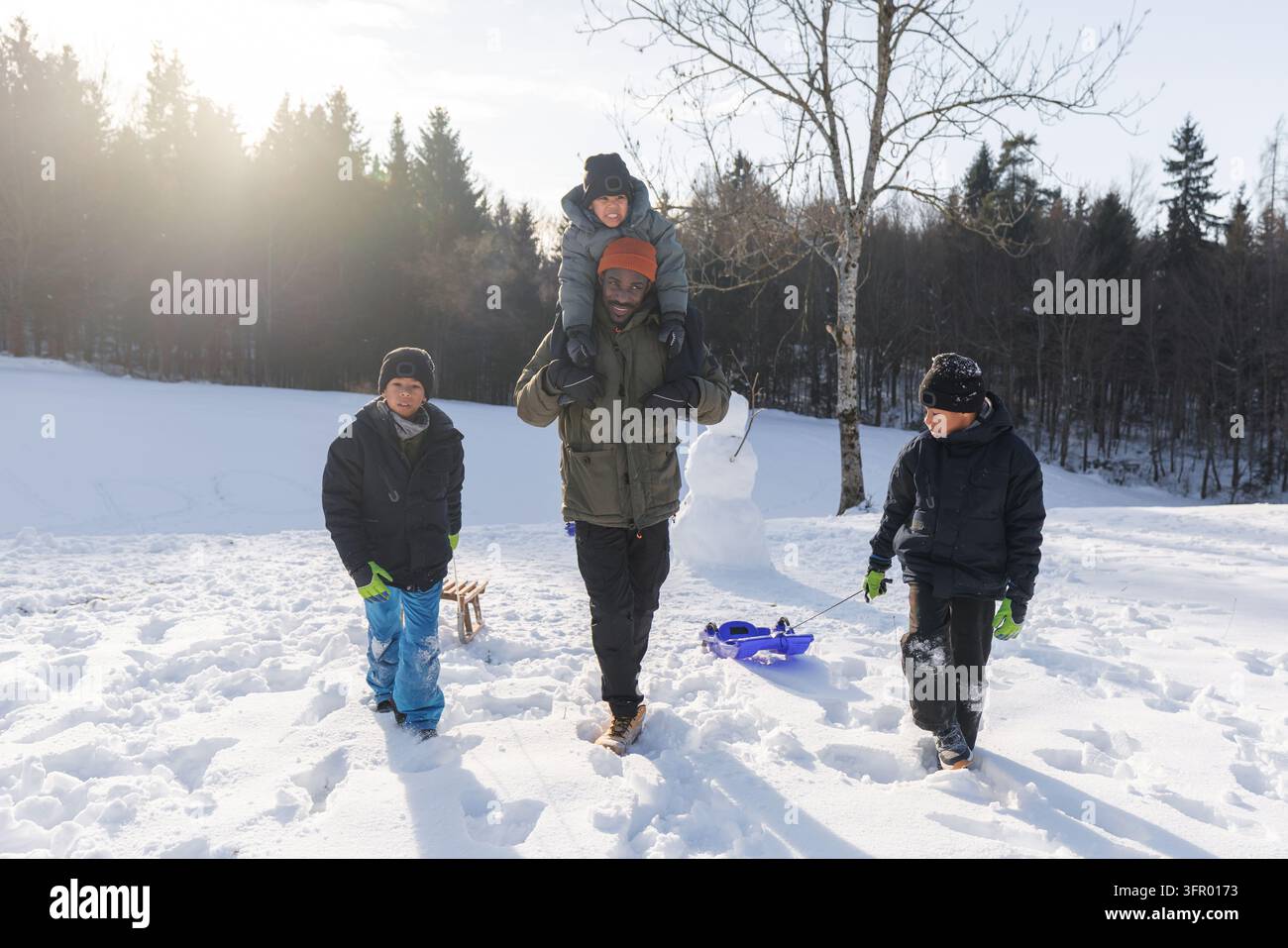 Vater und seine drei Söhne genießen die familiäre Gemeinschaft und unbeschwerte Kindheitsmomente, während sie verspielte Zeit in einer friedlichen Winterlandschaft verbringen. Stockfoto