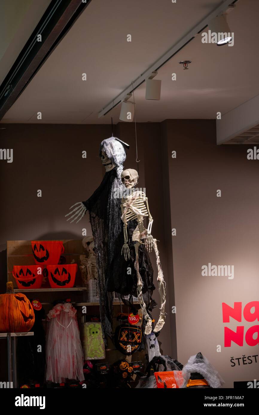 Halloween-Dekorationen, darunter hängende Skelette, ein Sensenmann, Kürbiskübel und gruselige Kostüme, die in einem Einzelhandelsgeschäft ausgestellt sind. Stockfoto