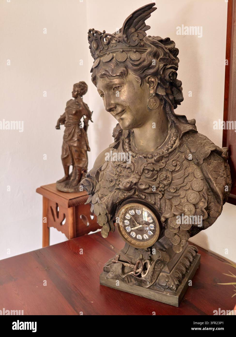 Ein antiker Bronzebüste, die eine klassische Figur darstellt, möglicherweise eine Göttin oder Kaiserin, mit einer integrierten Uhr auf ihrer Brust, die auf einem polierten Holz steht Stockfoto