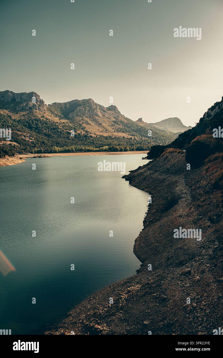 Ein ruhiges Landschaftsfoto, das einen ruhigen Bergsee mit klarem, grünlich-blauem Wasser zeigt, der rechts von einem trockenen, felsigen Ufer begrenzt wird. Im Bac Stockfoto