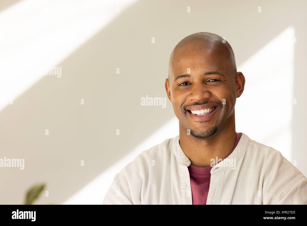 Afrikanischer Mann lächelt, trägt ein beiges Hemd über einem kastanienbraunen T-Shirt mit verschwommener Pflanze, Kopierraum Stockfoto