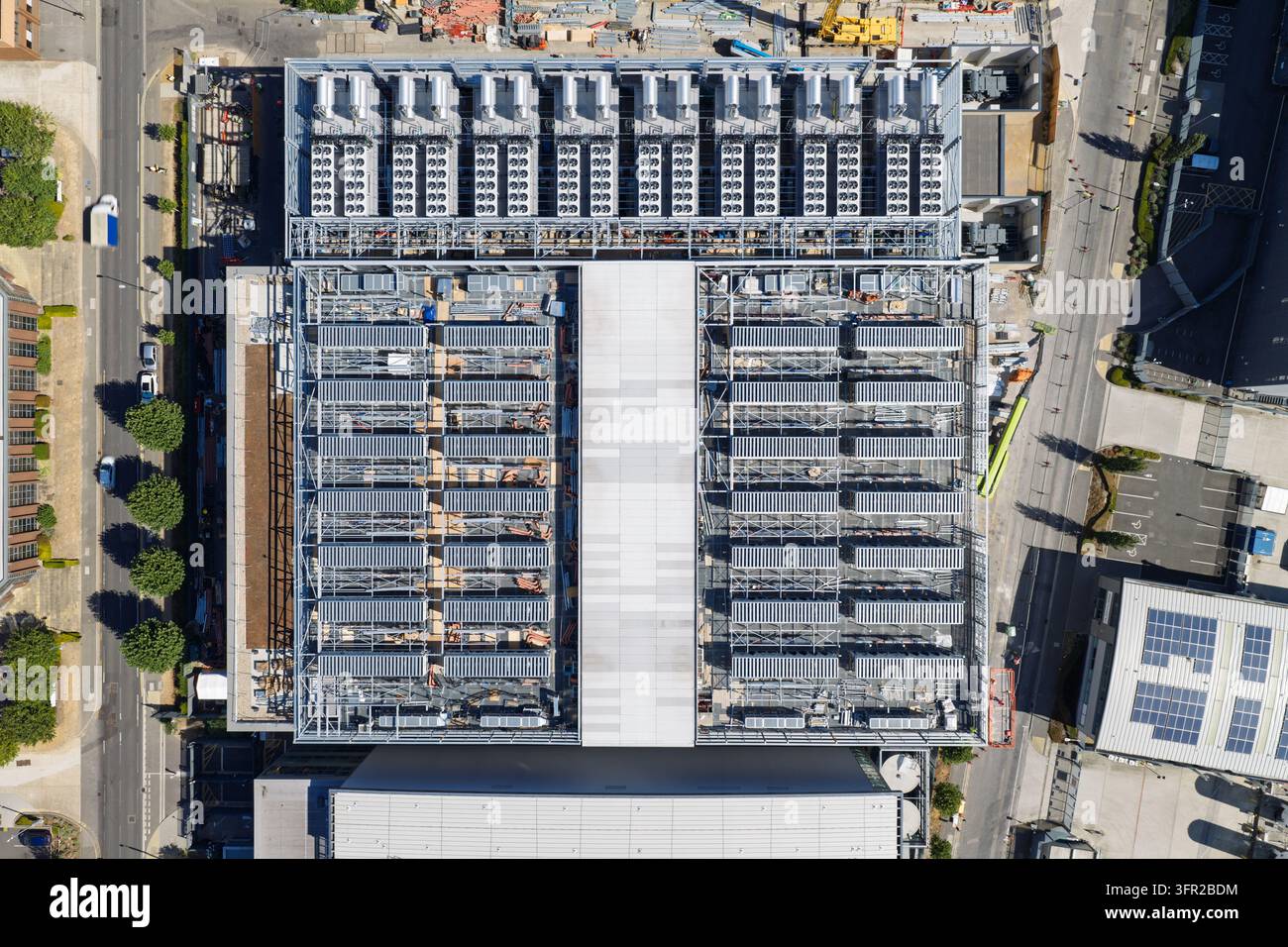 Großes industrielles Rechenzentrumsgebäude zeigt Reihen von Servergehäusen und Kühleinheiten auf dem Dach in einem städtischen Gebiet während des Tages mit klarem Schatten Stockfoto