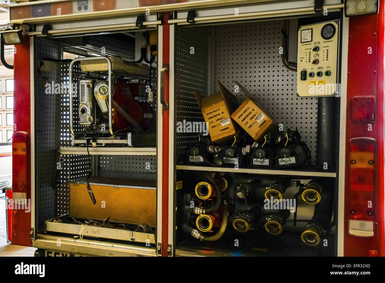 Offene Fächer eines roten Feuerwehrfahrzeugs zeigen Feuerlöschausrüstung, Schlauchkupplungen, Maschinen und technische Bedienelemente. Stockfoto
