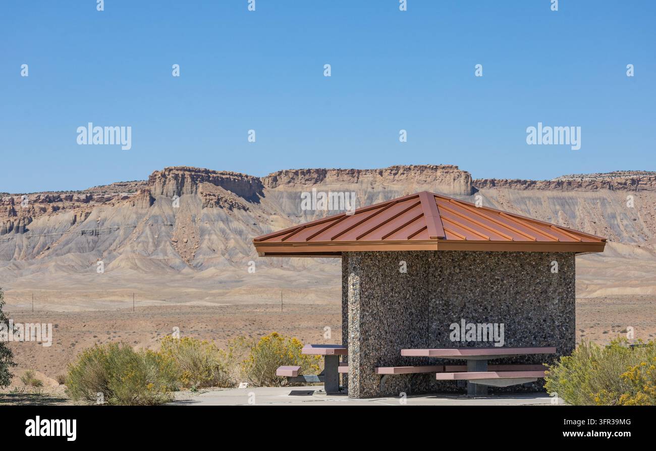 Überdachtes Straßenrand-Picknickunterstand mit Tischen und Bänken, umgeben von spärlicher Wüstenvegetation und geschichteten Felswänden in der Nähe von Crescent Junction, Utah. Stockfoto