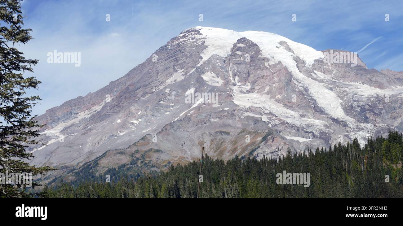 Mount-Rainier-Vulkan, der über immergrünen Wäldern aufragt und seinen schneebedeckten Gipfel und die Gletscherfelder in der Kaskadenkette zur Schau stellt. , Mount Rainier Stockfoto