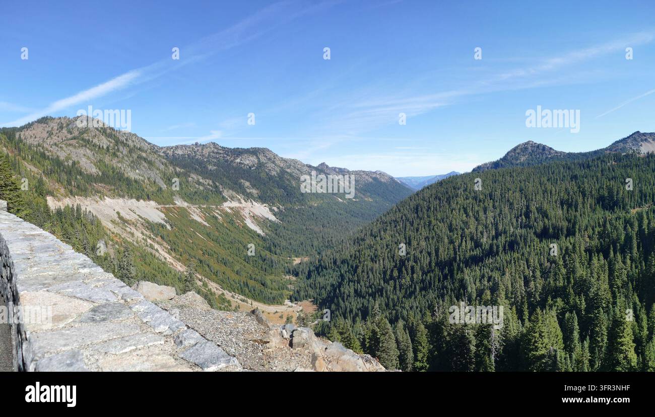 Ruhiges Bergtal mit einem dichten Kiefernwald, einer gewundenen Straße und einer Steinmauer unter einem klaren blauen Himmel. , Mount Rainier Nationalpark, Washingt Stockfoto