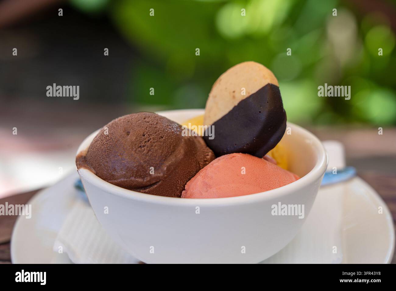 Kugeln aus Schokolade, Erdbeer- und Mangoeis mit Keksen in einer weißen Schüssel, Nahaufnahme Stockfoto